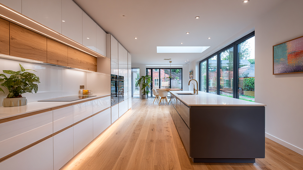 Cocina abierta moderna con isla central y acabados en blanco mate y madera cálida, integrada al comedor con luz natural.